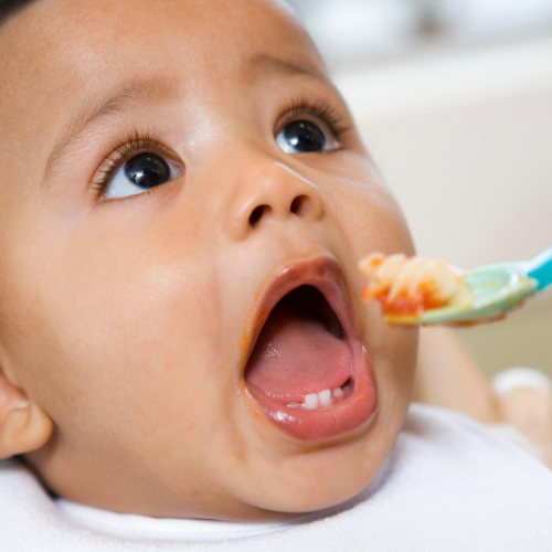 Baby opening mouth wide for a noodle.