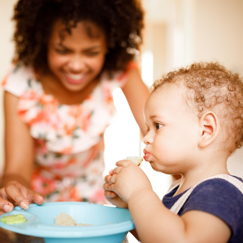 A baby holding finger foods and feeding himself.