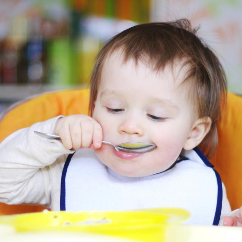 A baby holding a spoon and attempting to feed himself with it.